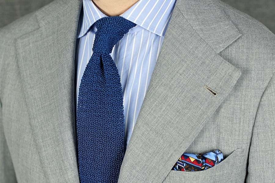 Costume gris clair et cravate en maille bleue.