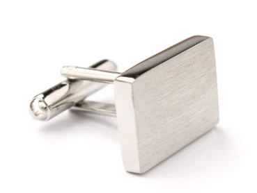Vue détaillée d’un bouton de manchette rectangulaire en métal argenté, au design minimaliste et à la finition brossée. Son système de fermeture pivotant assure à la fois praticité et maintien. Un accessoire intemporel, sobre et moderne, idéal pour compléter une tenue formelle avec discrétion et sophistication.