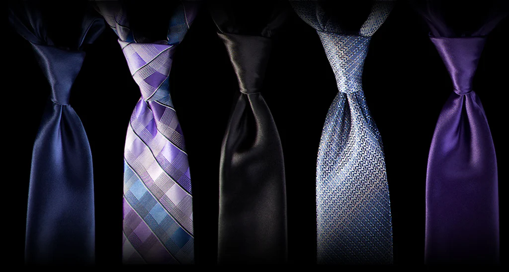Une sélection de cinq cravates aux teintes de bleu, violet et noir, présentant différents styles allant de l'uni au quadrillé et aux motifs géométriques.
