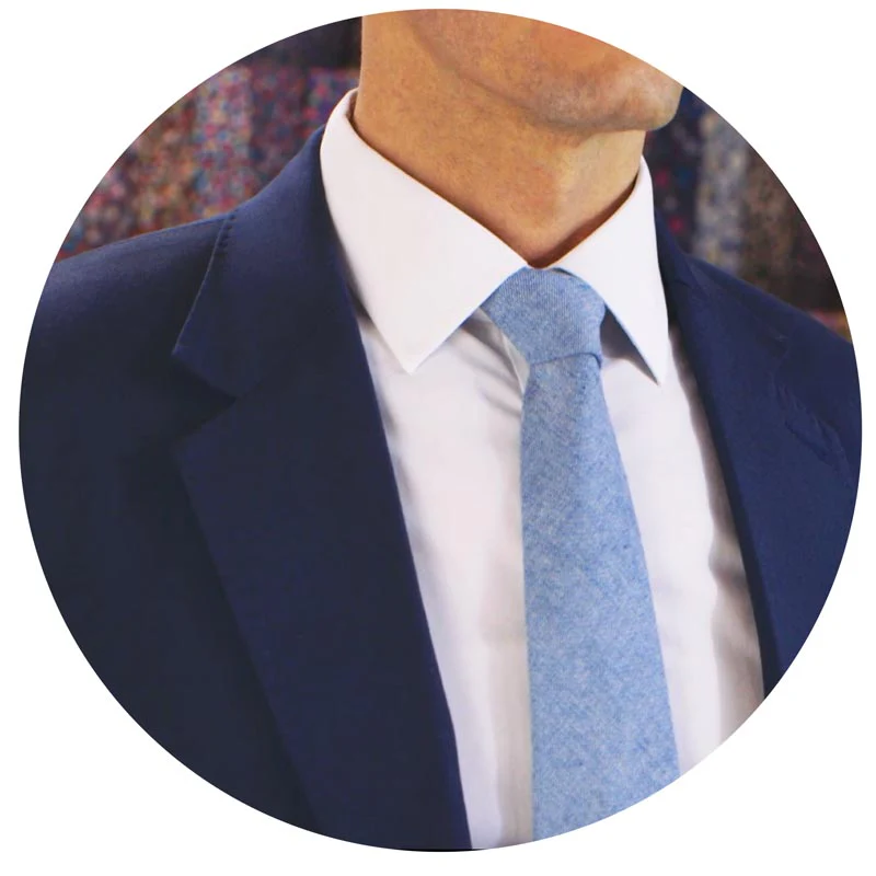 Un homme en costume bleu marine avec une chemise blanche et une cravate bleu clair unie. Le nœud de cravate est simple et bien centré, offrant une apparence professionnelle et sobre.