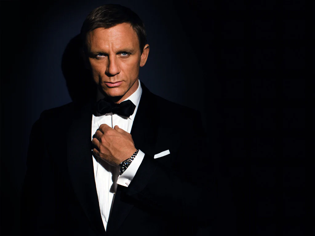 L'homme porte un smoking noir impeccable (black tie). Il est vêtu d'une veste à revers en soie ou satin, d'une chemise blanche à plastron plissé et d'un nœud papillon noir noué avec soin.