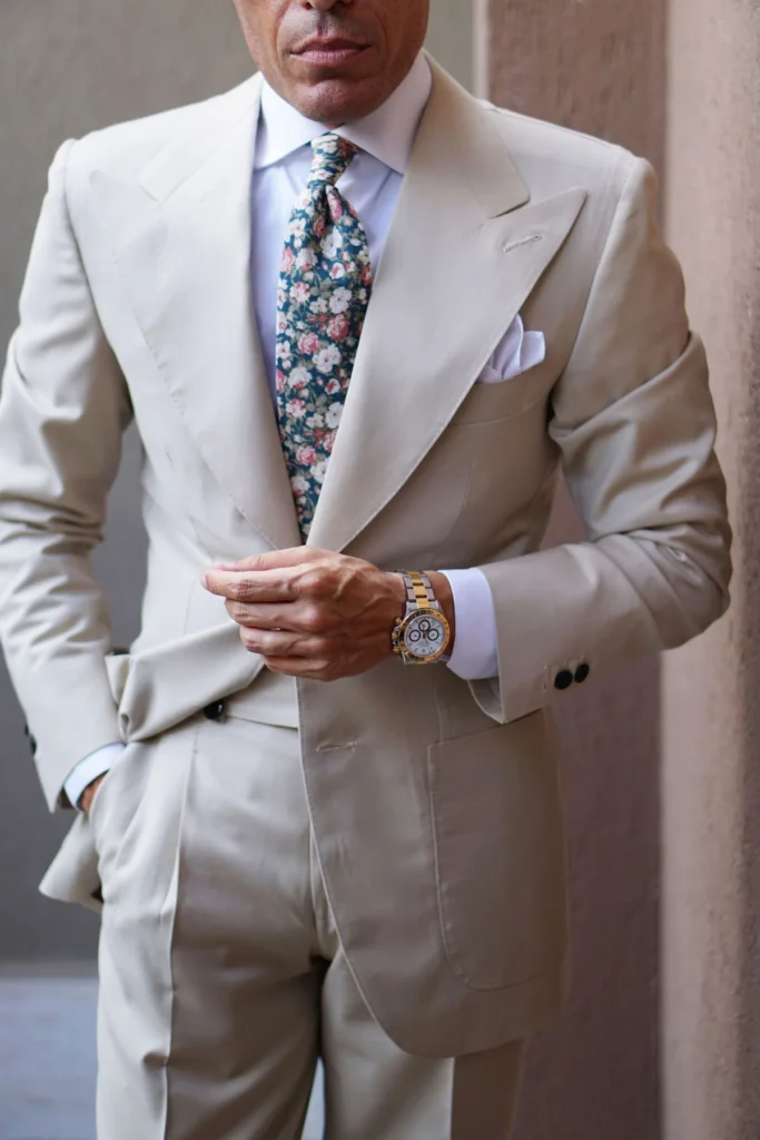 Costume beige clair à la coupe fluide, associé à une chemise blanche immaculée et une cravate florale délicate. L’ensemble dégage une élégance naturelle et raffinée, sublimée par des accessoires sobres et une attitude assurée.